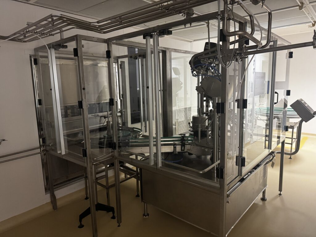 Línea de llenado y taponado de botellas BOC Edwards bajo una cubierta protectora de cristal, con mesas giratorias y cinta transportadora