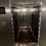 Getinge sterilizer with the vertical sliding door open, showing the chamber and the cart rails
