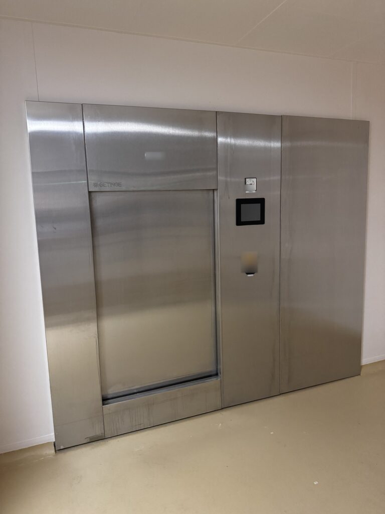 Esterilizador de vapor de doble puerta de Getinge integrado en una mampara de sala limpia, con pantalla táctil y manómetro de la cámara